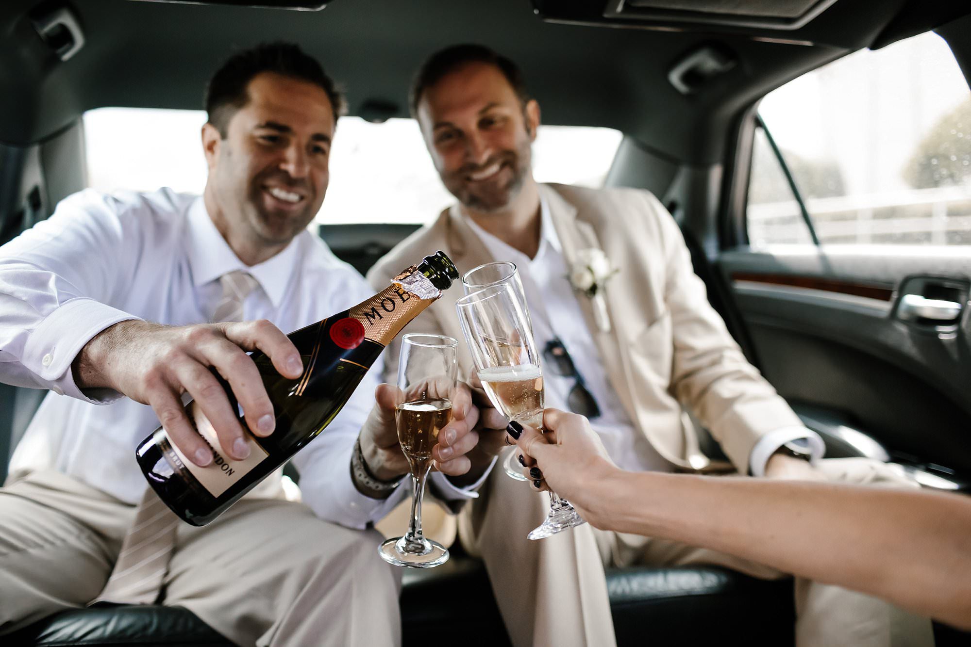 Groom pouring champagne in limo for bestman
