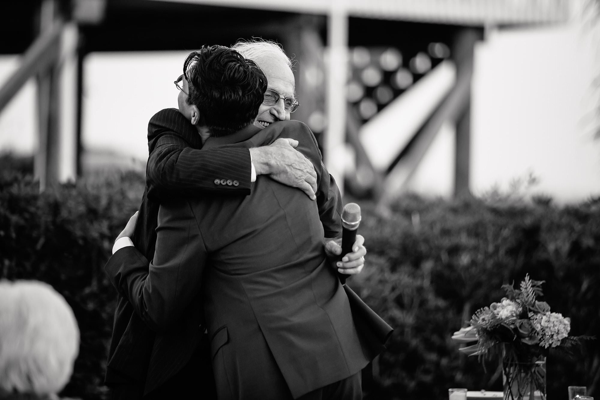 Groom hug grandfather at outdoor reception around pool at Aisle of Palms beach house on St. George Island