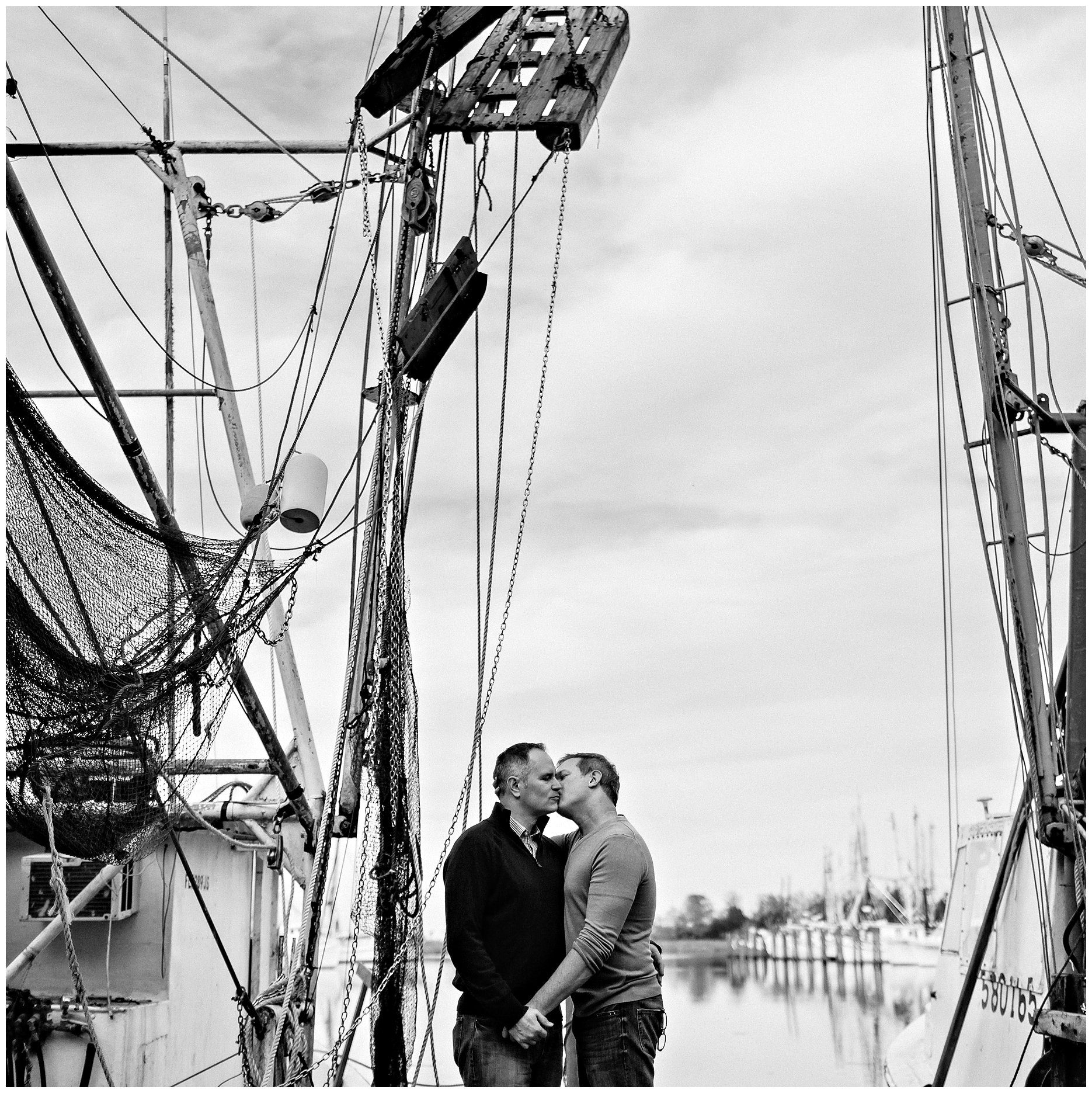 Black and white portrait of couple embracing between shrimp boats in the marina located in downtown Apalachicola Florida