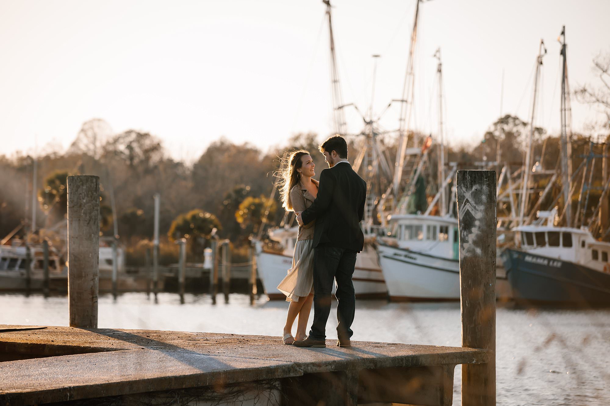 Megan and Turner embracing on the dock backlit by the sun hair blowing in the wind