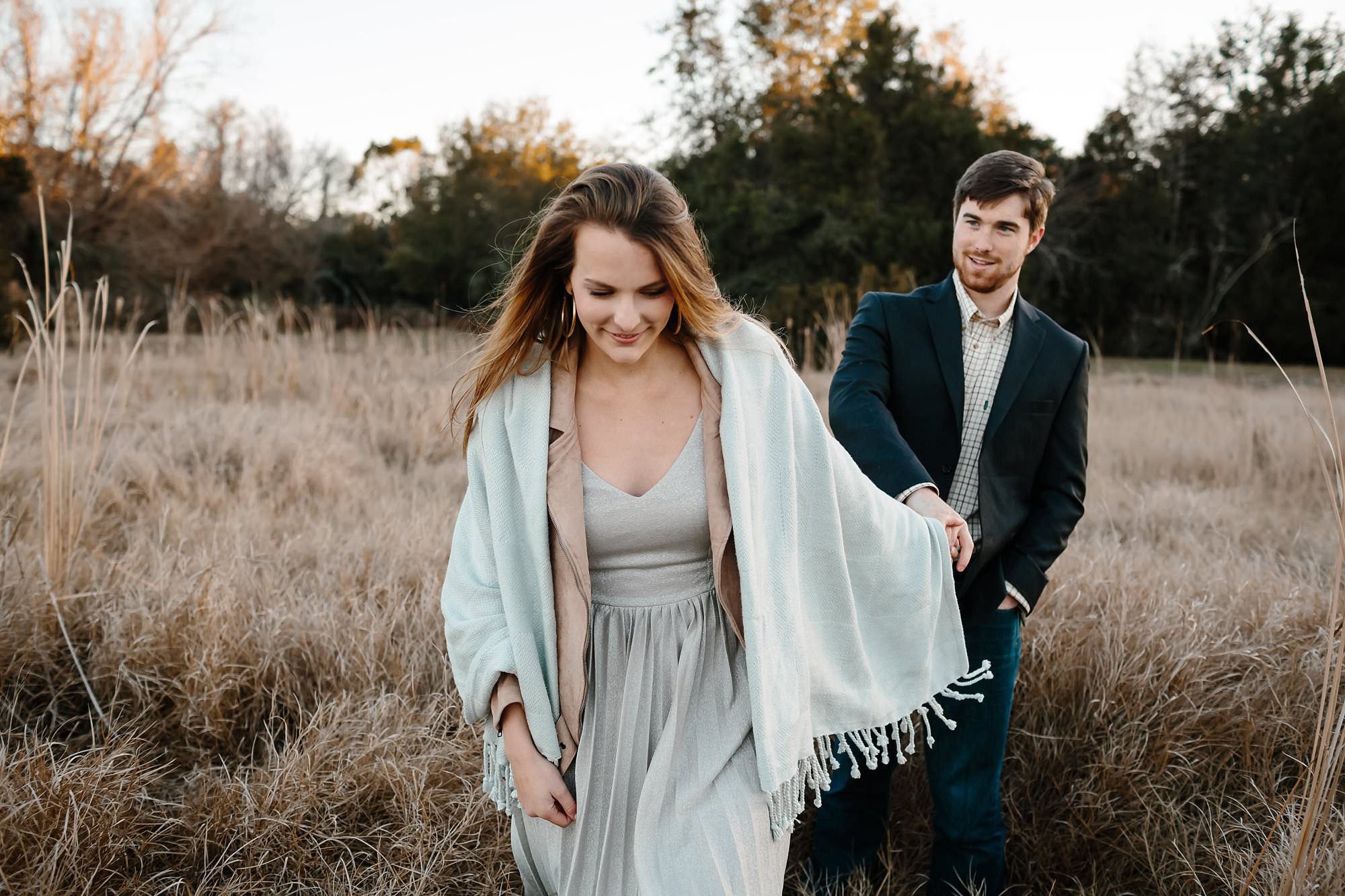 Megan in a short sundress wrapped in a blanket leading Turner out of a field of tall grass