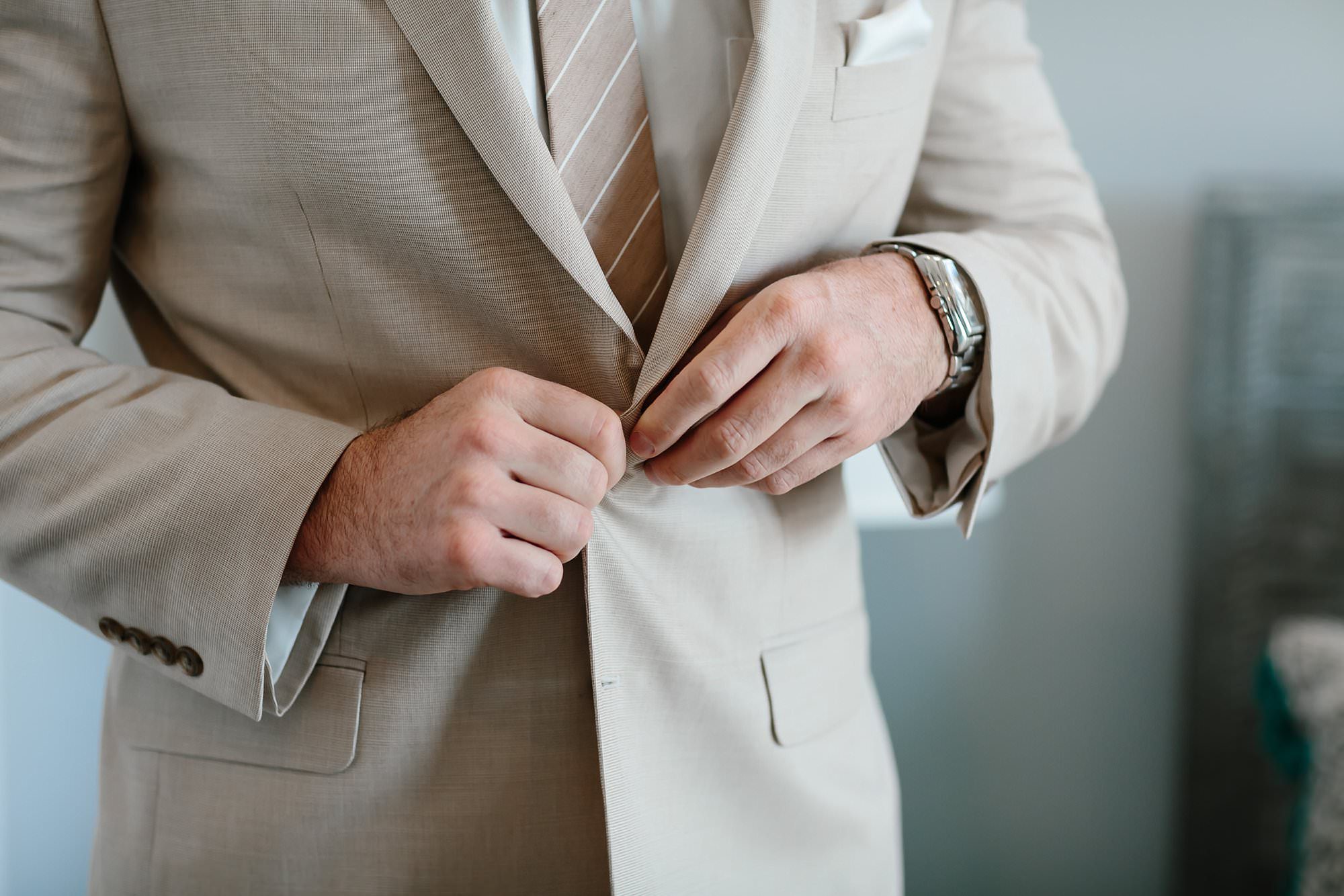 Close up of Groom buttoning jacket