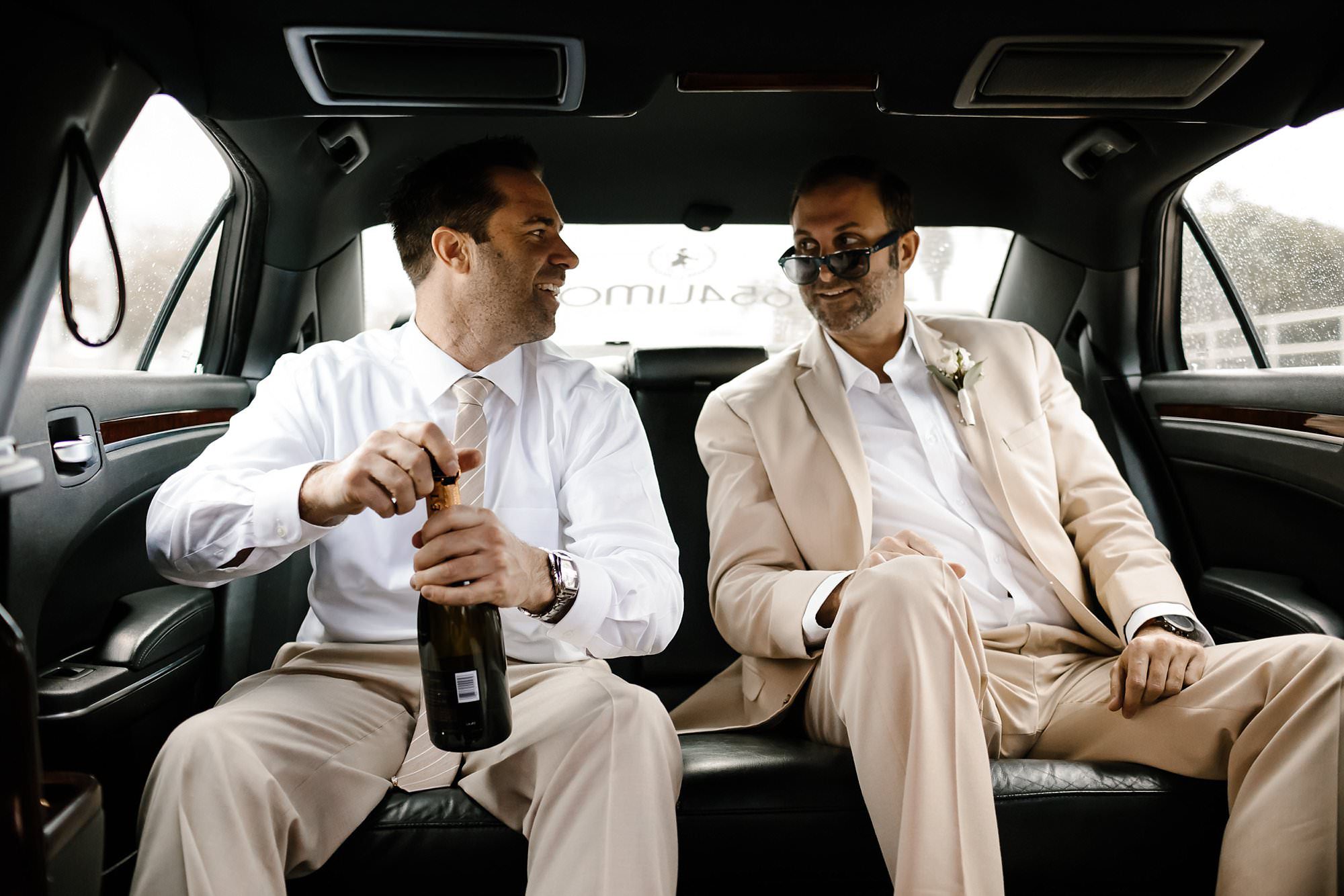 Groom and best man in limo opening champagne