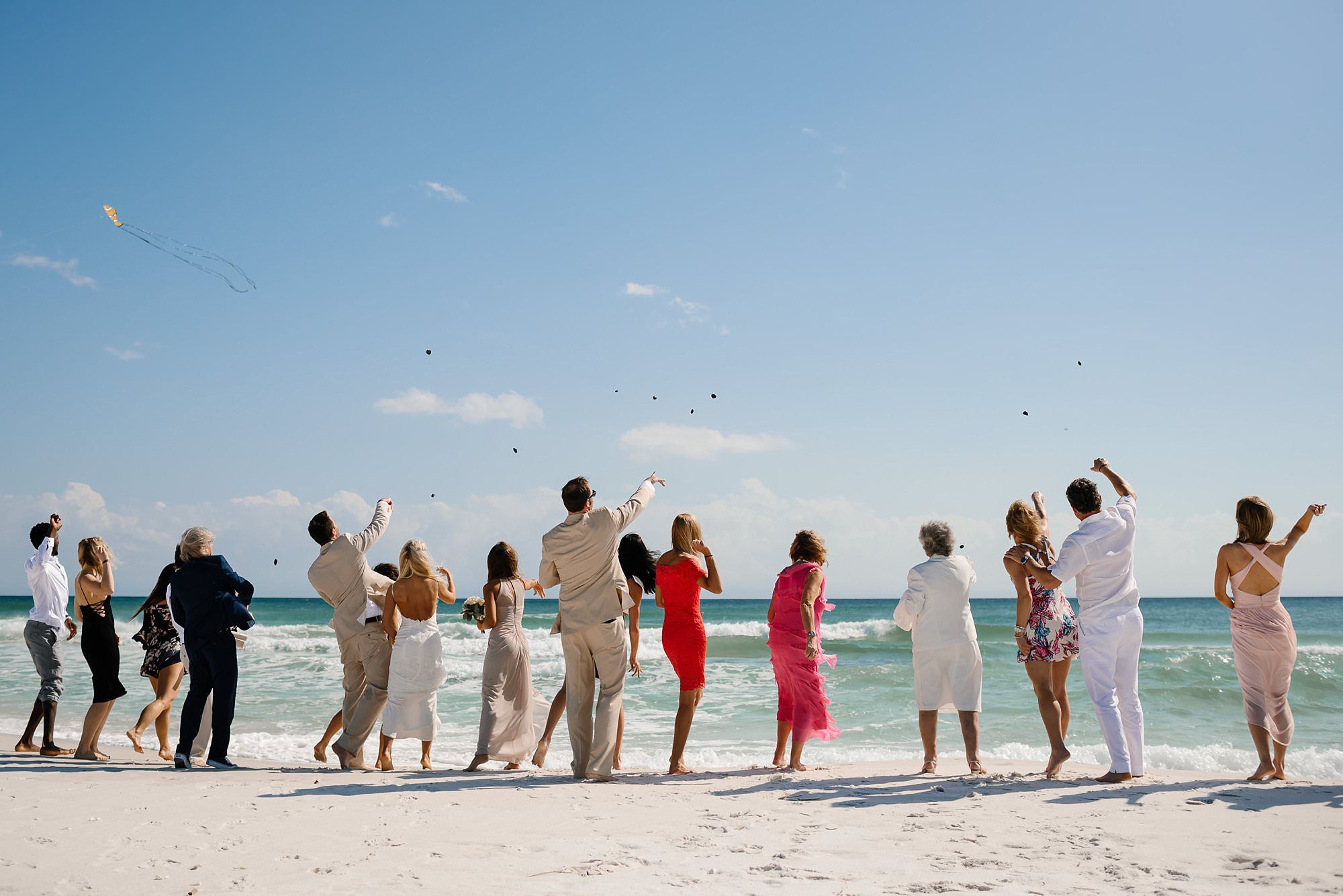 Wedding party and guests standing at the waters edge tossing shells into the Gulf of Mexico in Destin Florida