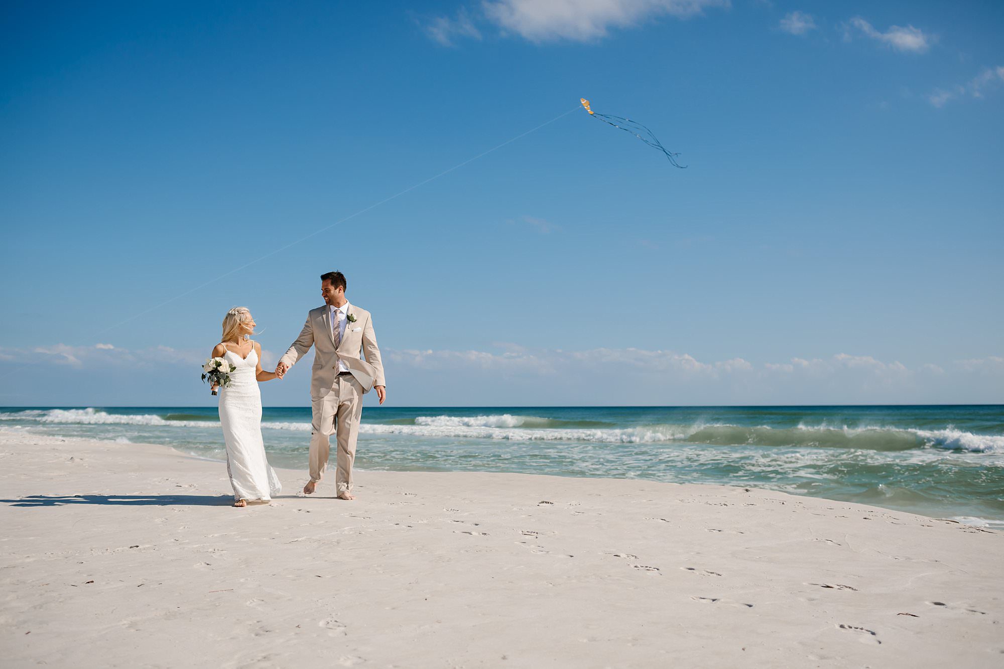 Bride and Groom walking along the waters edge while a yellow kite flys over Gulf of Mexico