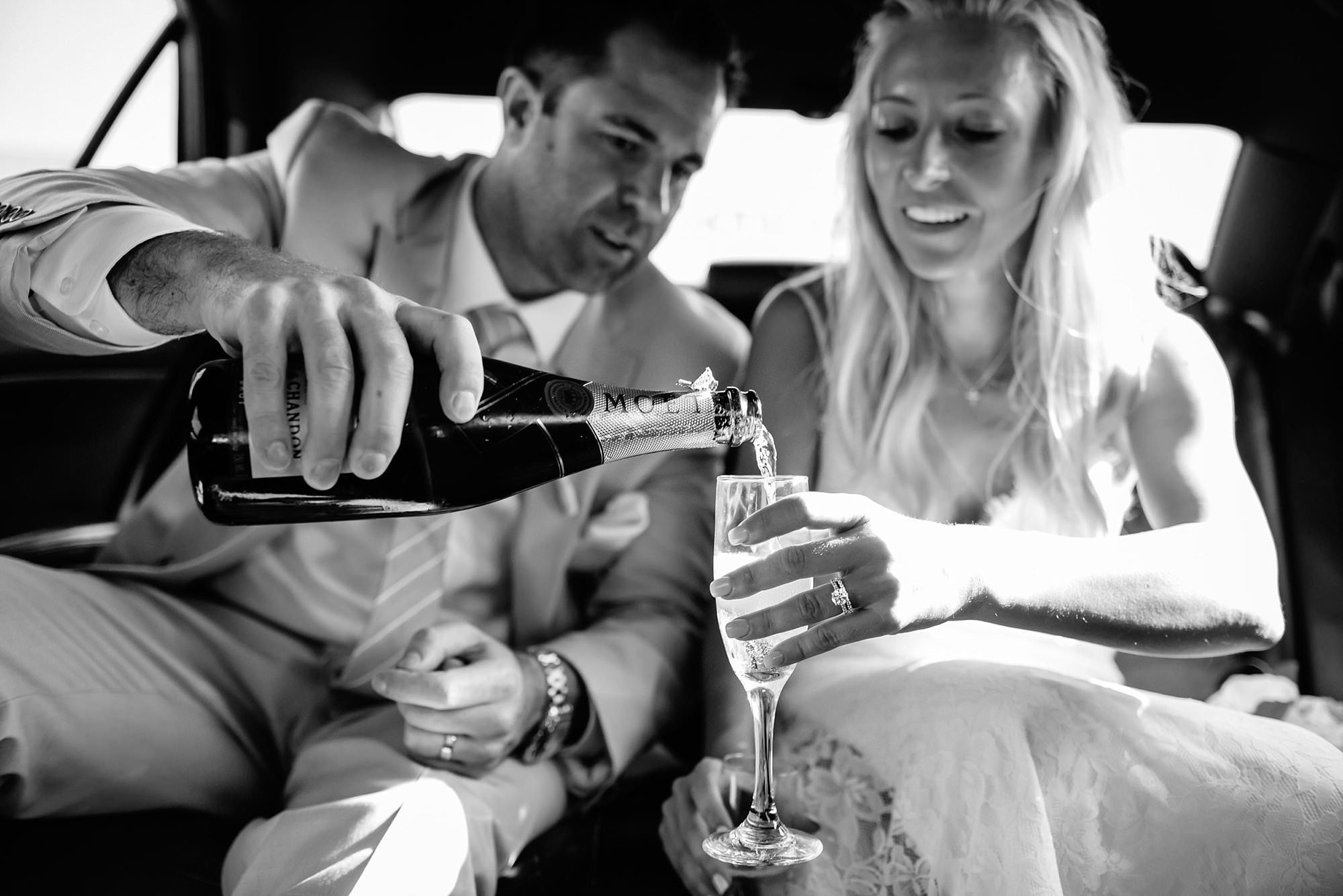 Black and White portrait of groom pouring champagne for bride in back of 654 limo