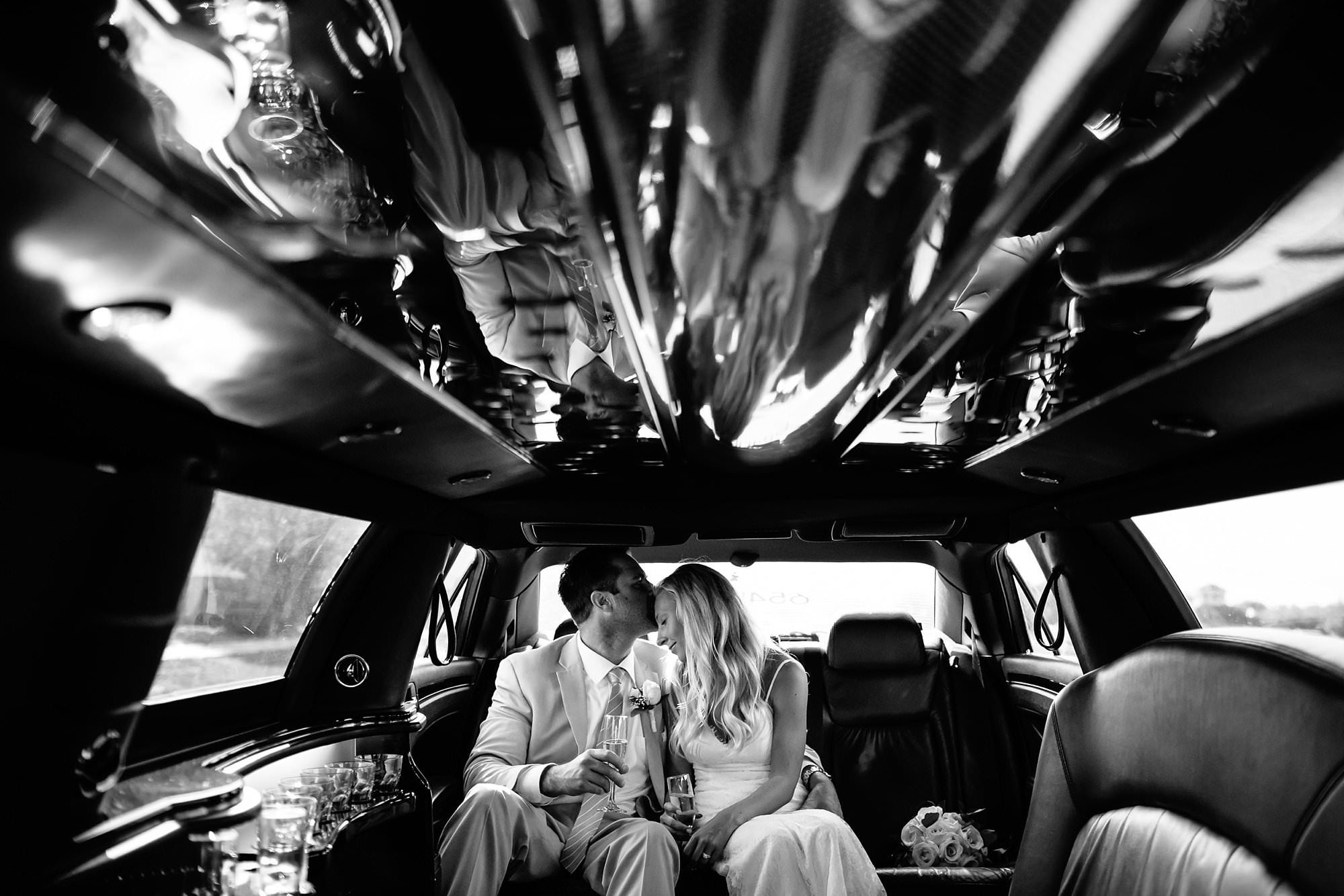Black and White portrait of groom kissing bride on forehead in back of 654 limo