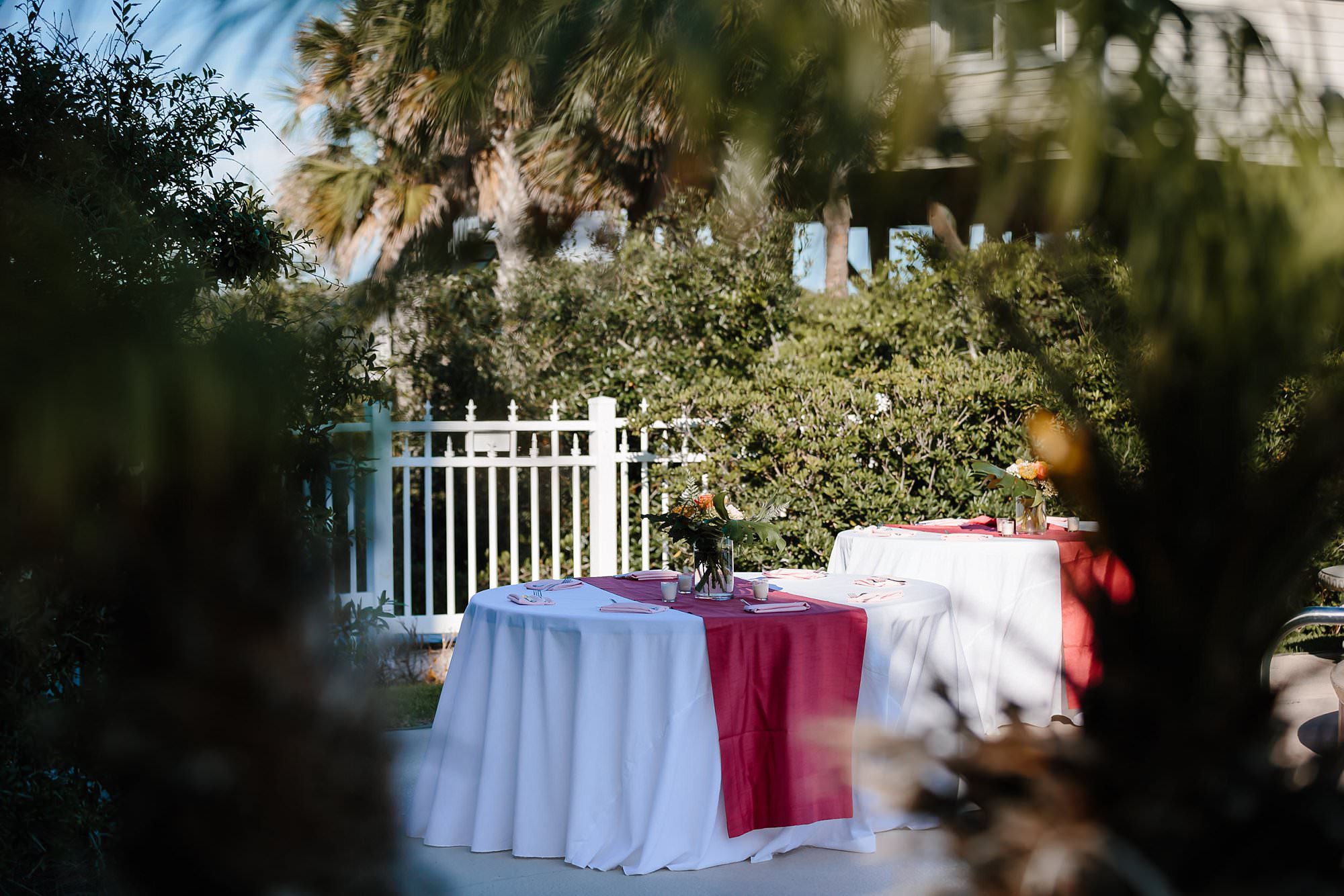 Outdoor round tables set for wedding reception with tropical flowers and bright coral runners