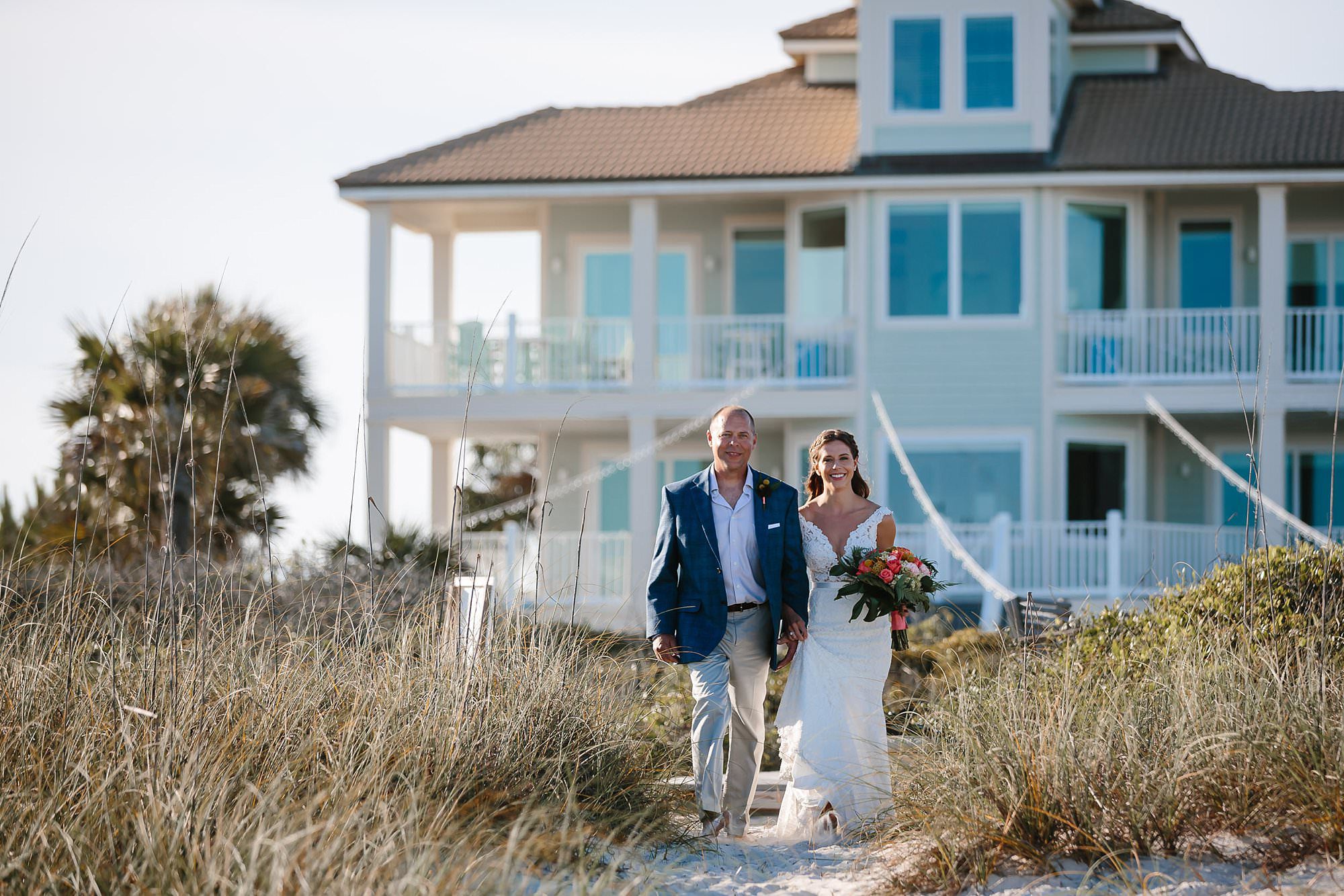 Bride and father walking through sea oats to beach ceremony