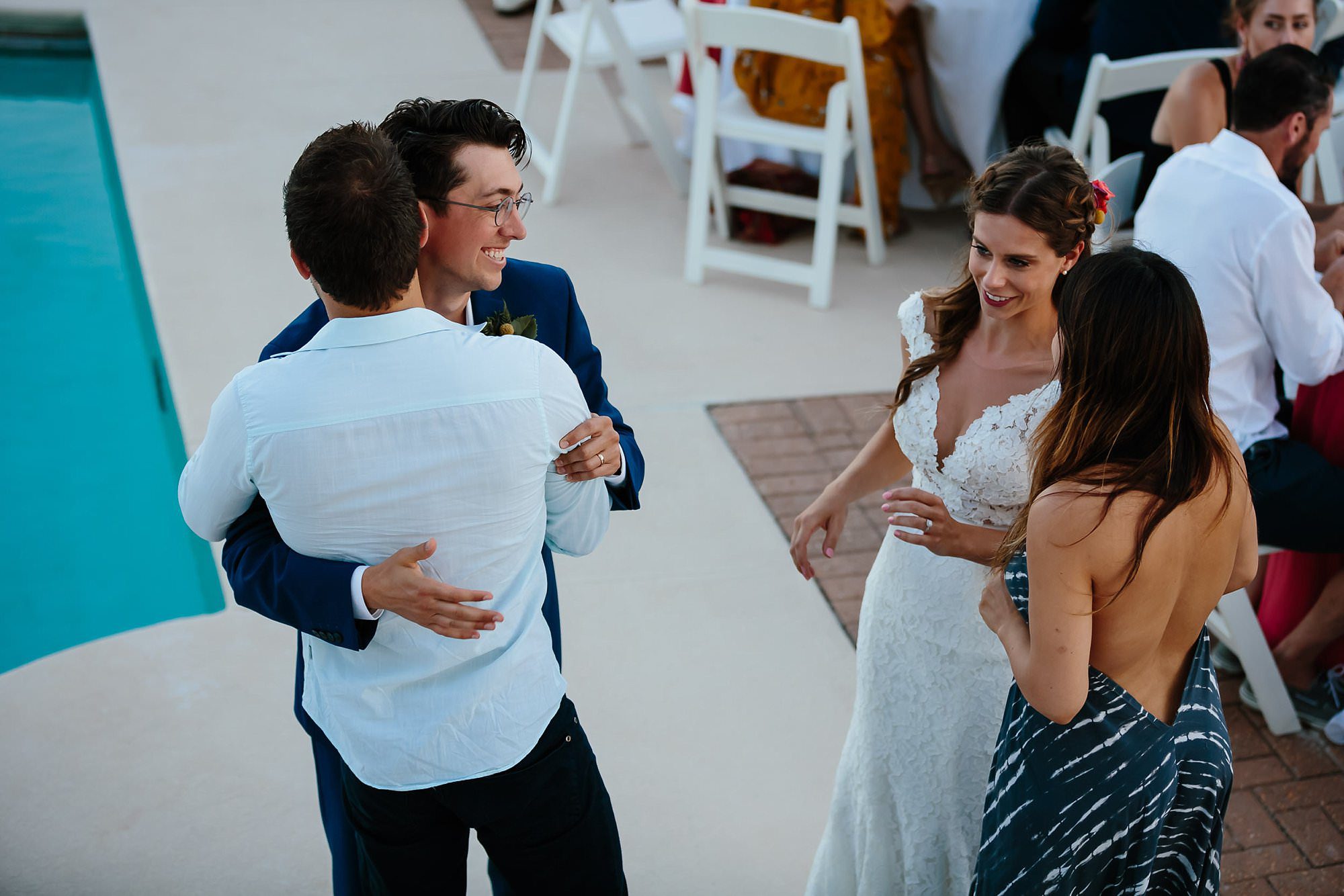 Bride and groom hug guests at outdoor reception around pool at Aisle of Palms beach house on St. George Island