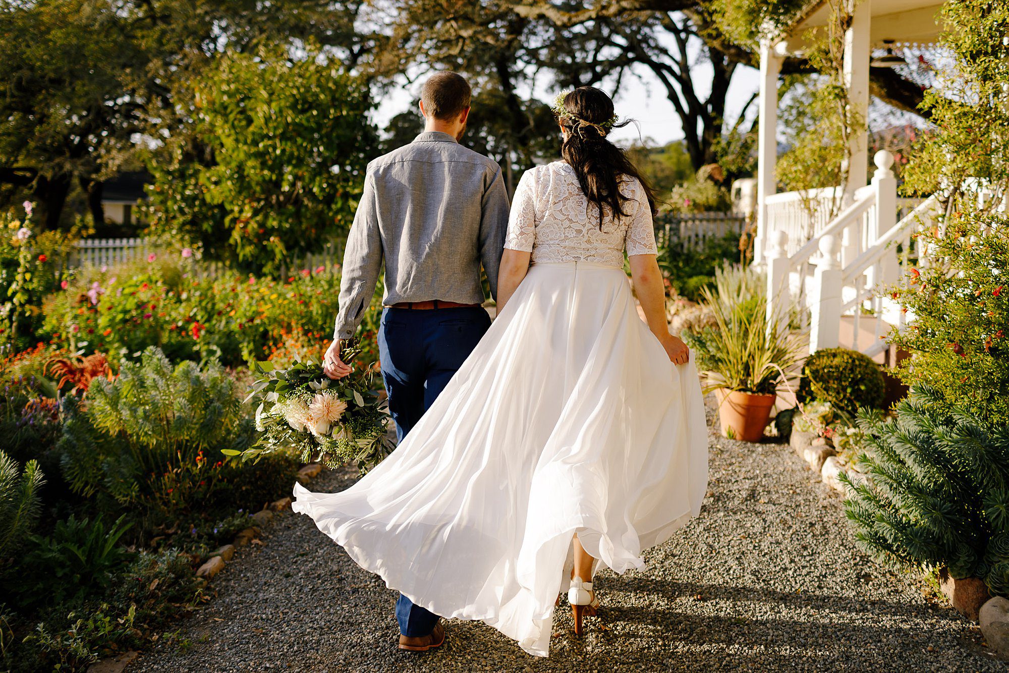 Angie and Tyler walking away with her dress blowing in the wind in front of building at Beltane Ranch 