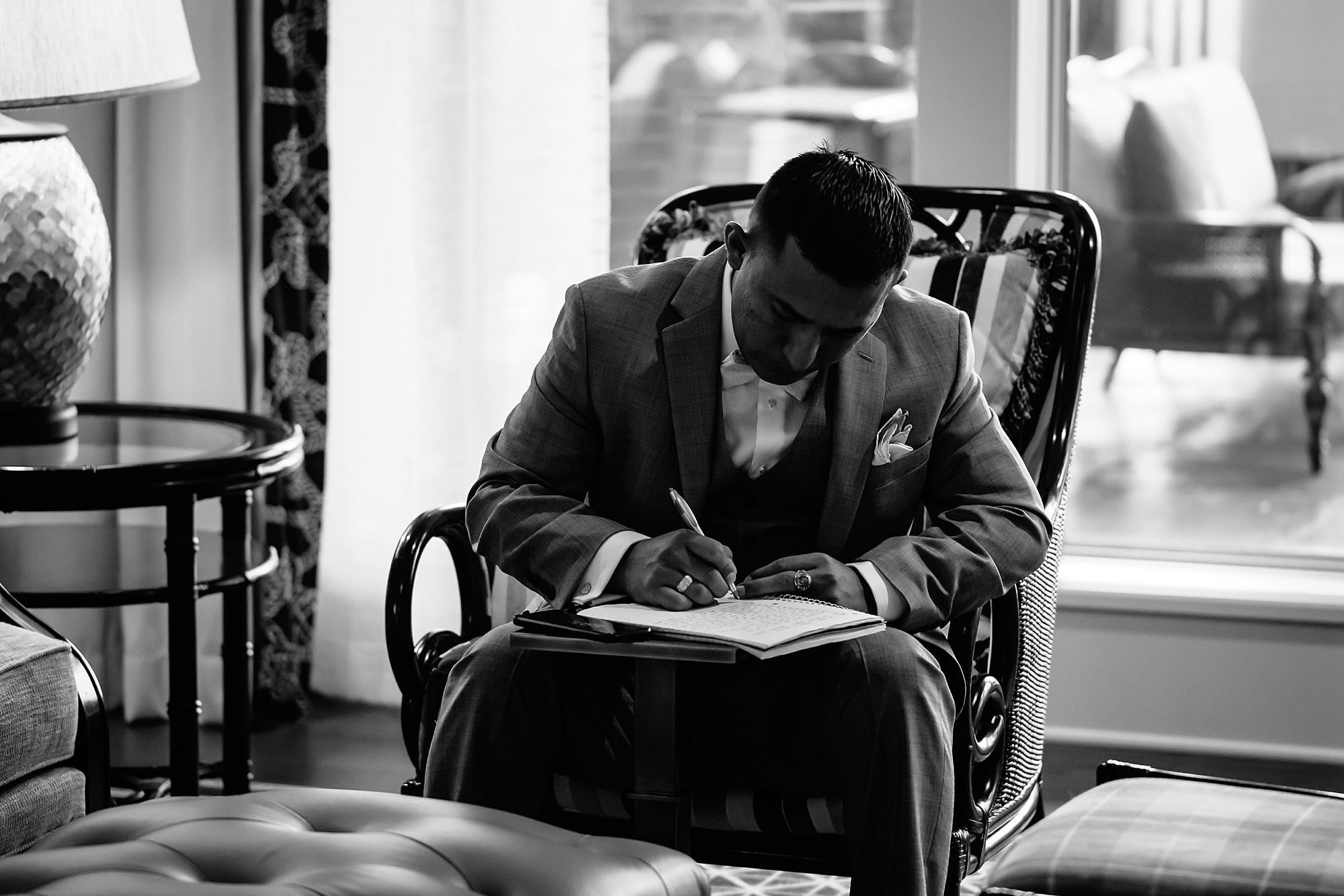 Black and white of groom writing letter to his bride 