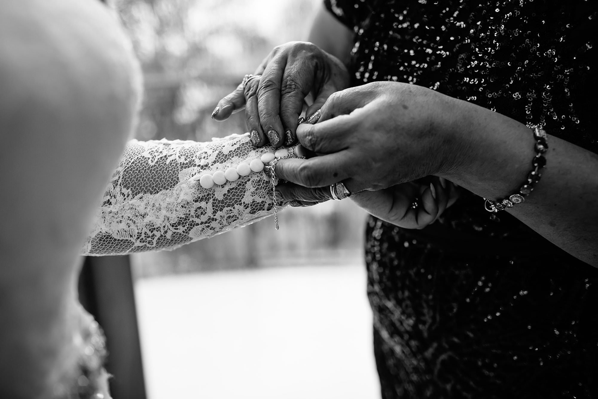 Black and white close up of brides mom putting on brides bracelets 