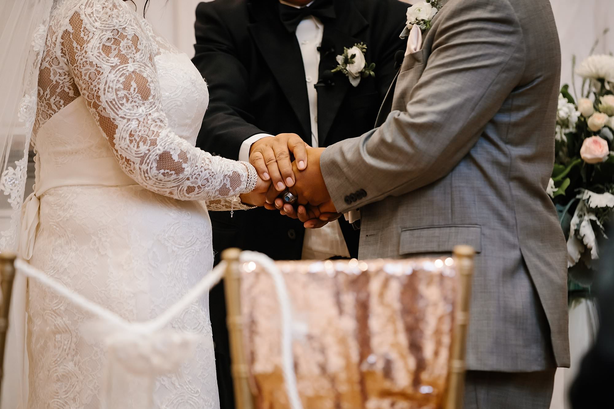 Close up of pastors hands covering bride and grooms hands during prayer 