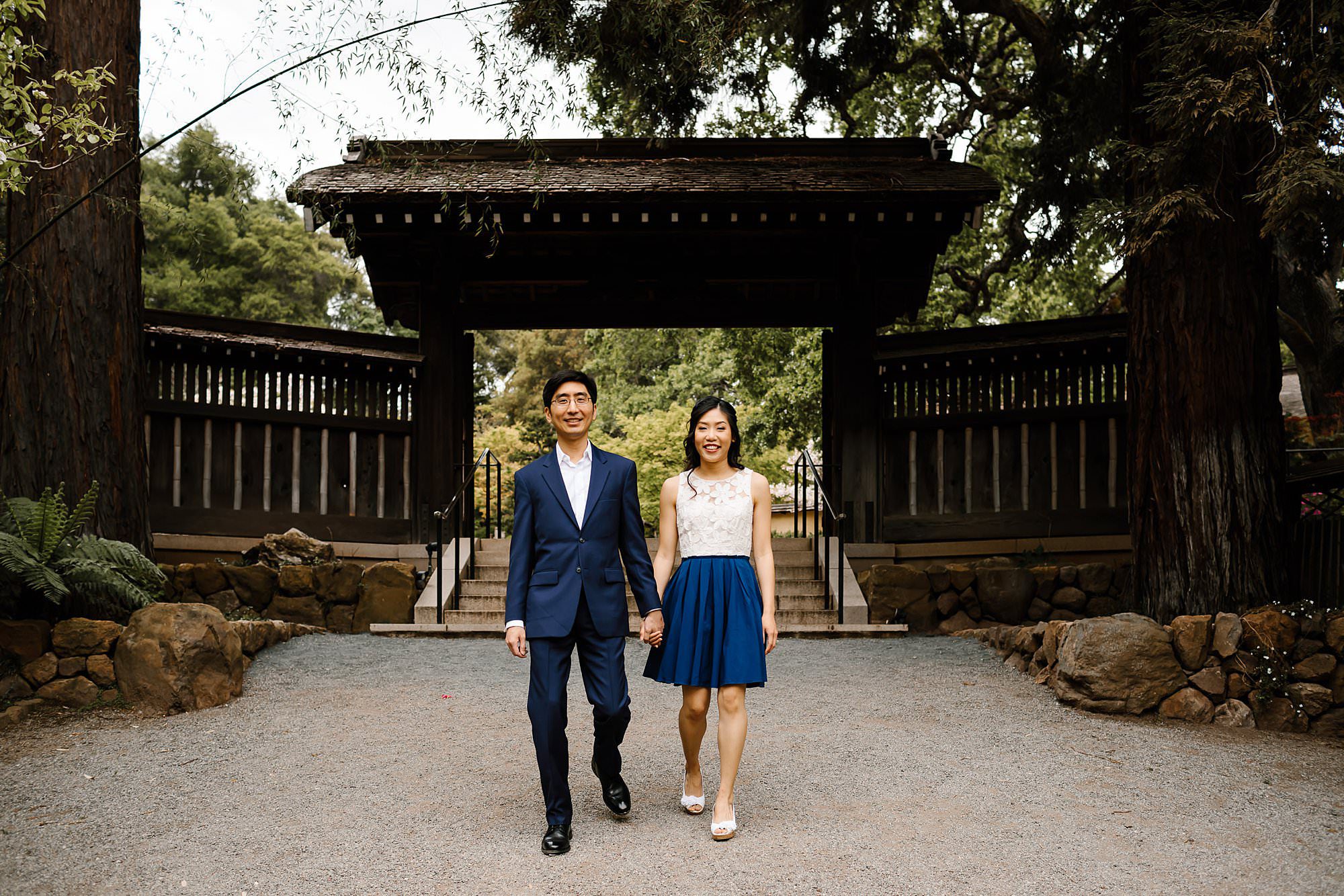 Couple holding hands walking towards camera in front of gates at Hakone Estate and Gardens