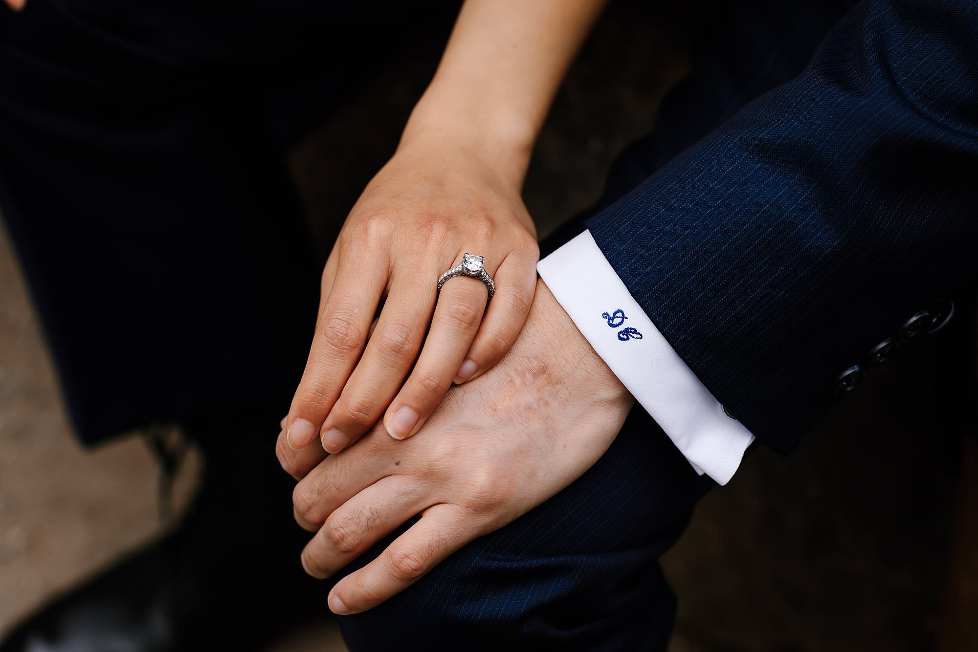 Close up of engaged couples hand showing engagement ring and grooms embroidered cuffs