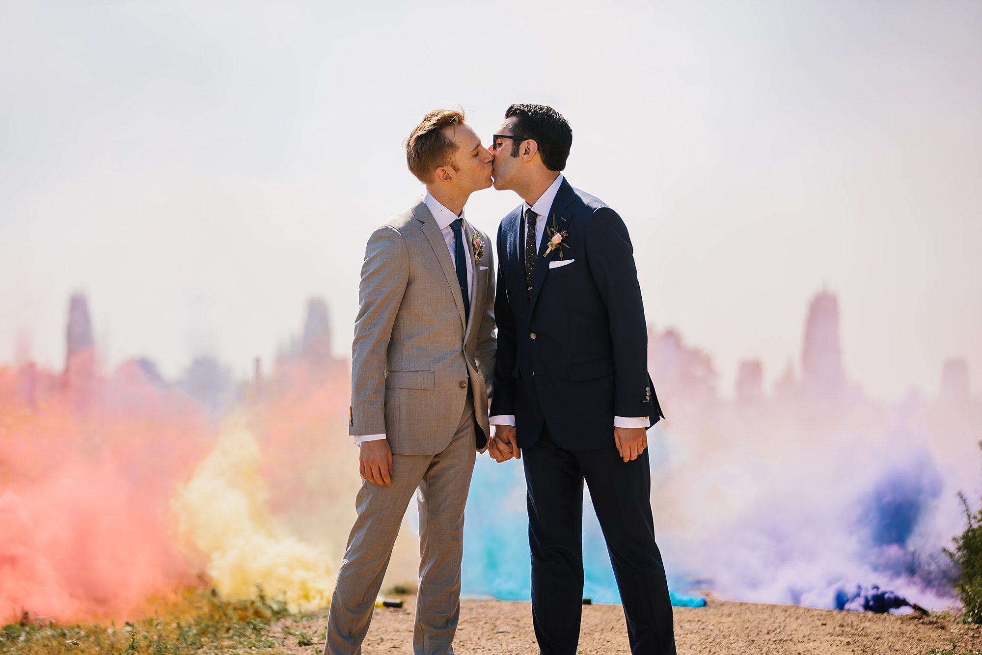 Cold burning rainbow smoke bombs on the ground behind two grooms kissing in the vineyard at Vintners Inn in Santa Rosa Ca