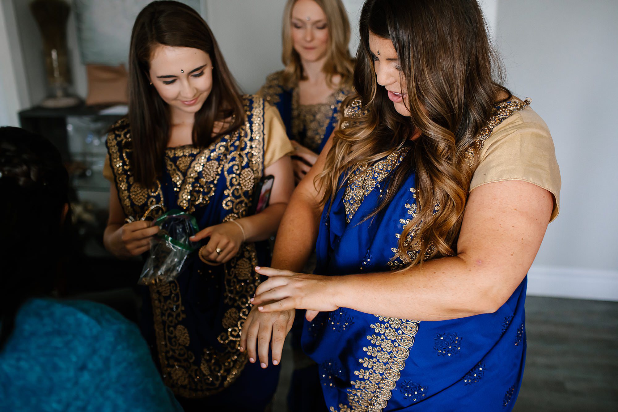 Bridesmaids in royal blue and gold saree's putting on gold bangles