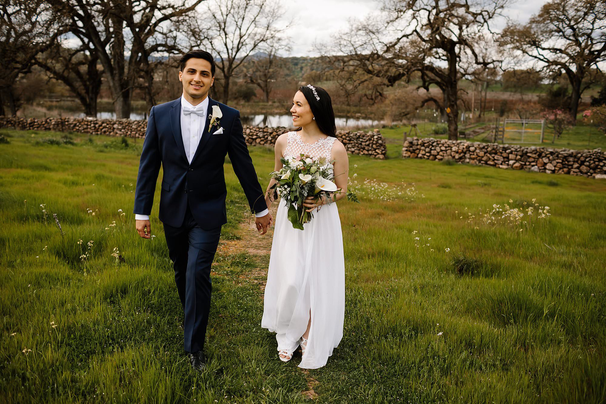 Bride and groom explore the grounds near the rock wall at their Beltane Ranch elopement