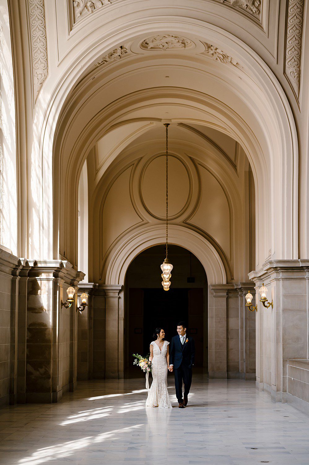 Bride and groom holding hands on the 4th floor of San Francisco City Hall before their wedding