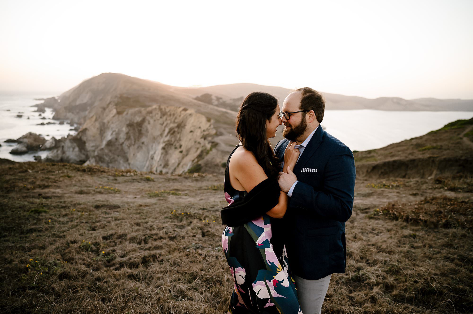 Engaged couple embracing on top of the cliffs on a sunset hike to Chimney Rock in Pt Reyes