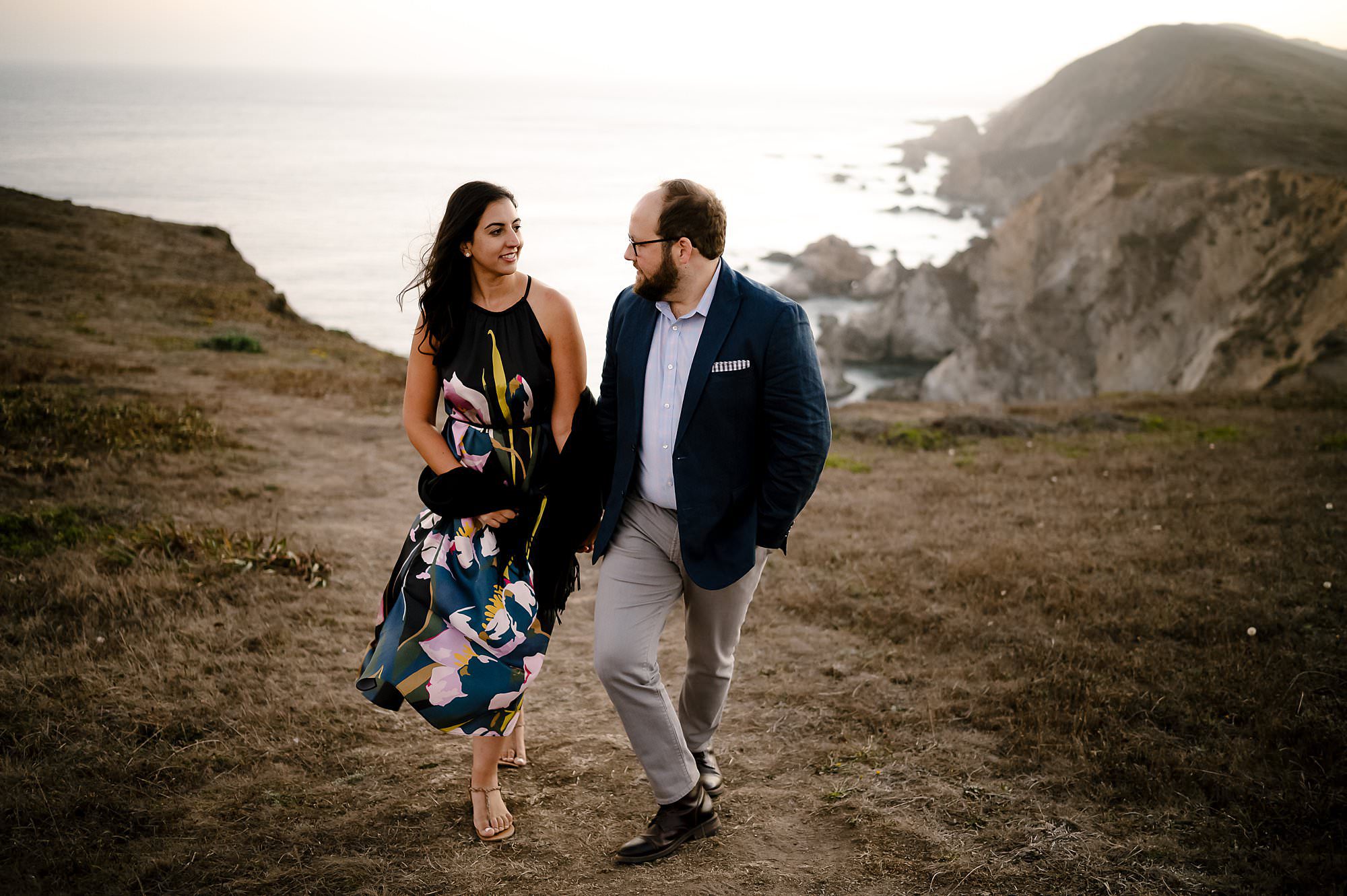 Engaged couple walking along the cliff side on a sunset hike to Chimney Rock in Pt Reyes