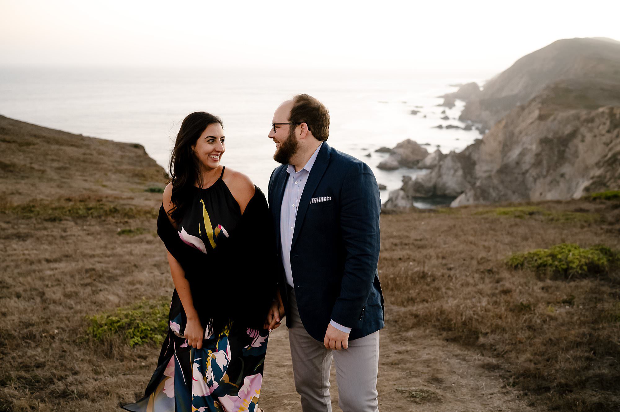 Engaged couple walking along the cliff side on a sunset hike to Chimney Rock in Pt Reyes