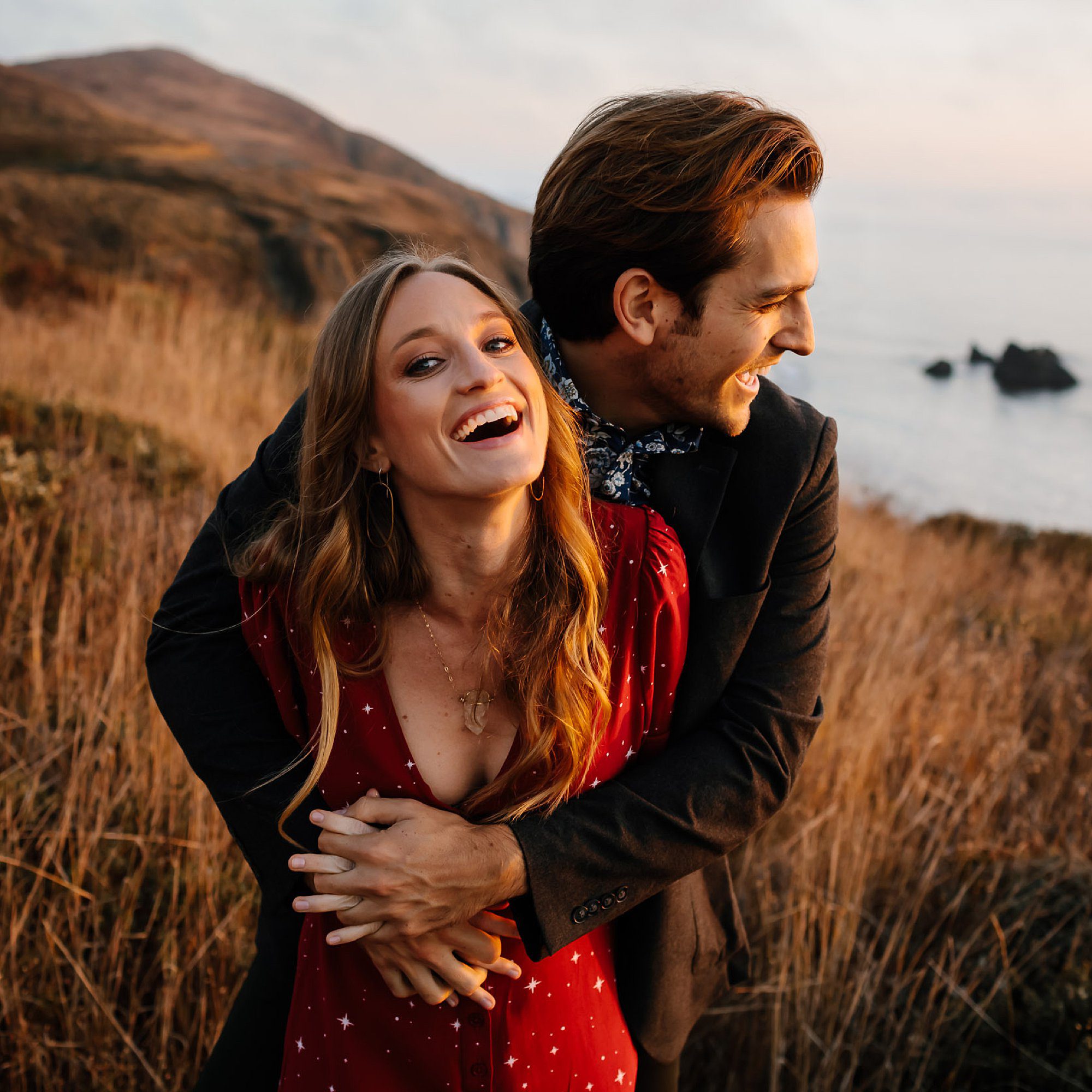 Austin and Casie laughing and embracing in the tall grasses on the cliffs above Goat Rock Beach in Jenner CA