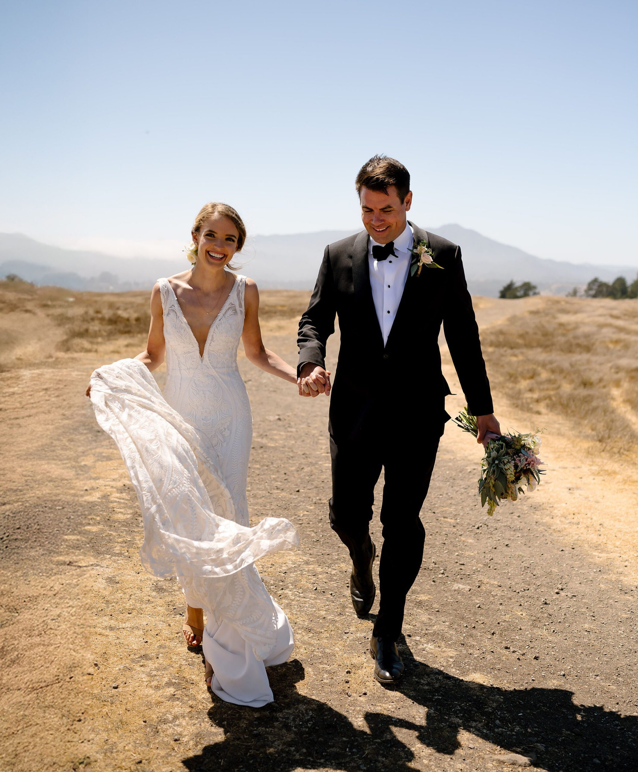 Amanda and Elliot hold hands while running down the path on top of Tiburon Ridge on the way to their Landmark Art and Garden Center wedding
