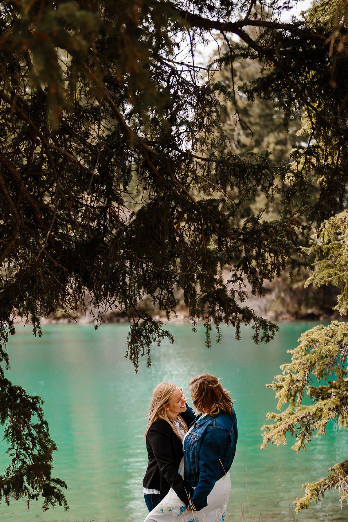Michelle and Hollie embracing under the tree at a Jasper lake in the Rocky Mountains